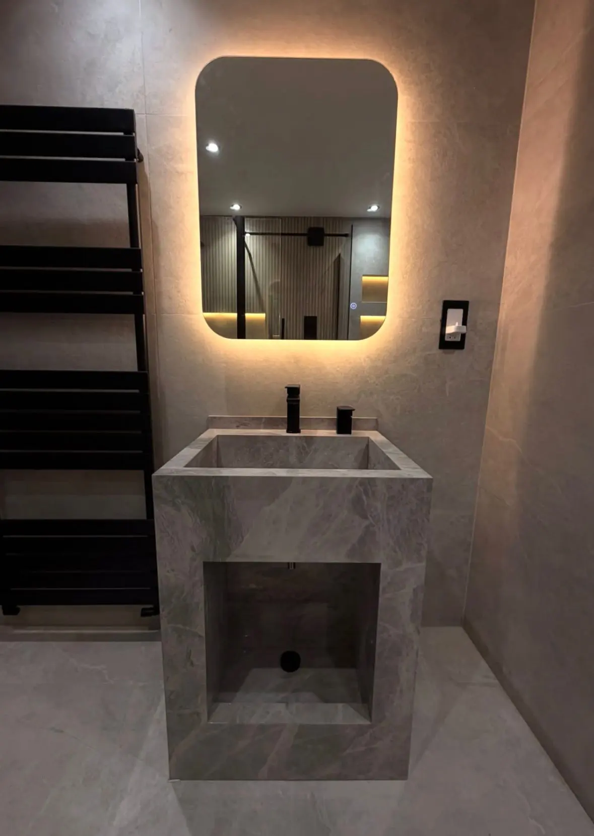 Bathroom with a backlit rounded mirror, a stone wash basin and a black heated towel rail