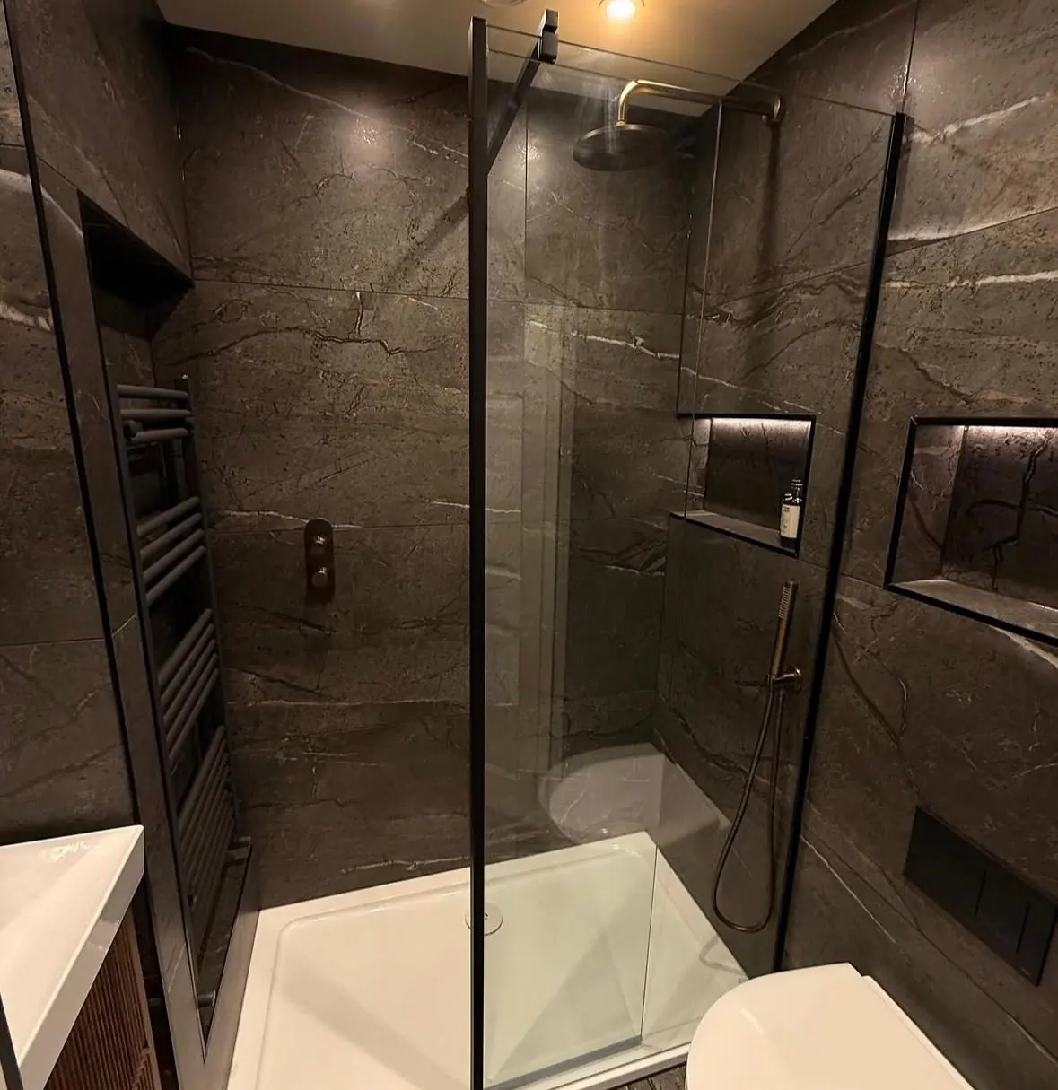 Walk-in shower with a black-framed glass screen, a rainfall head and lit alcoves